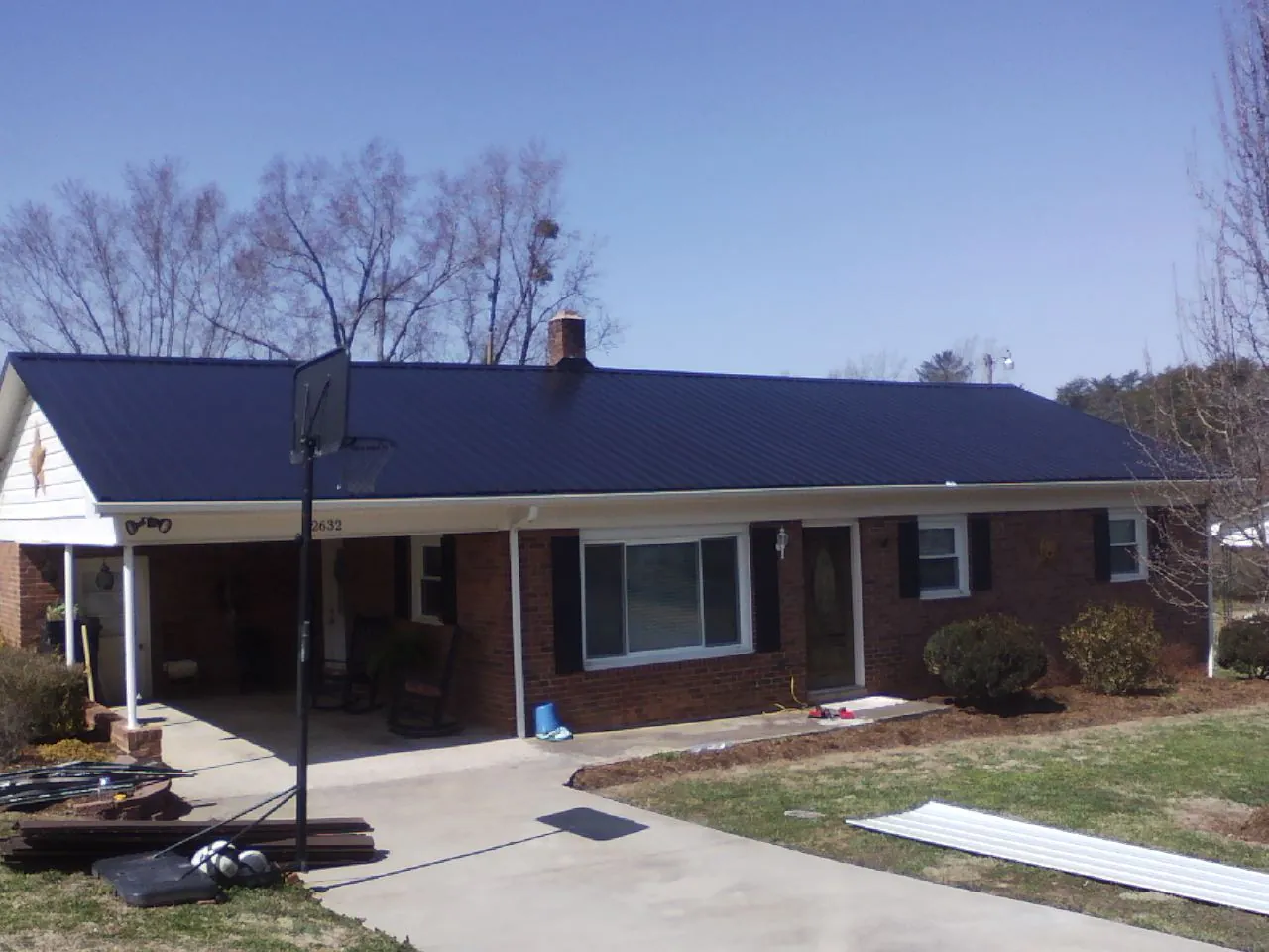 Finished dark blue metal roof on a brick ranch with a carport in Tow