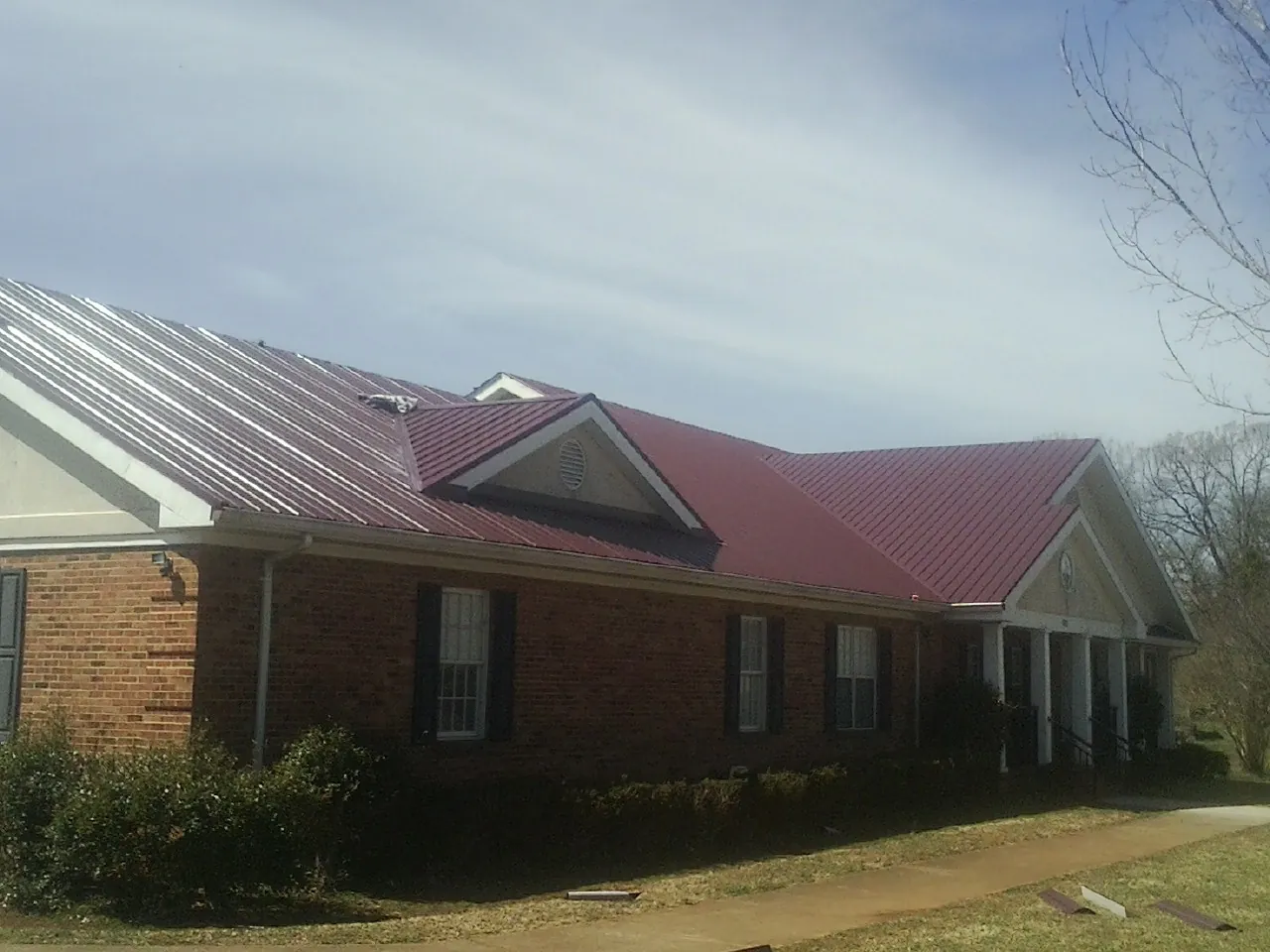 Red metal roof with gabled entries on a long brick building, from a Hail Damage Roof Repair job in Tow