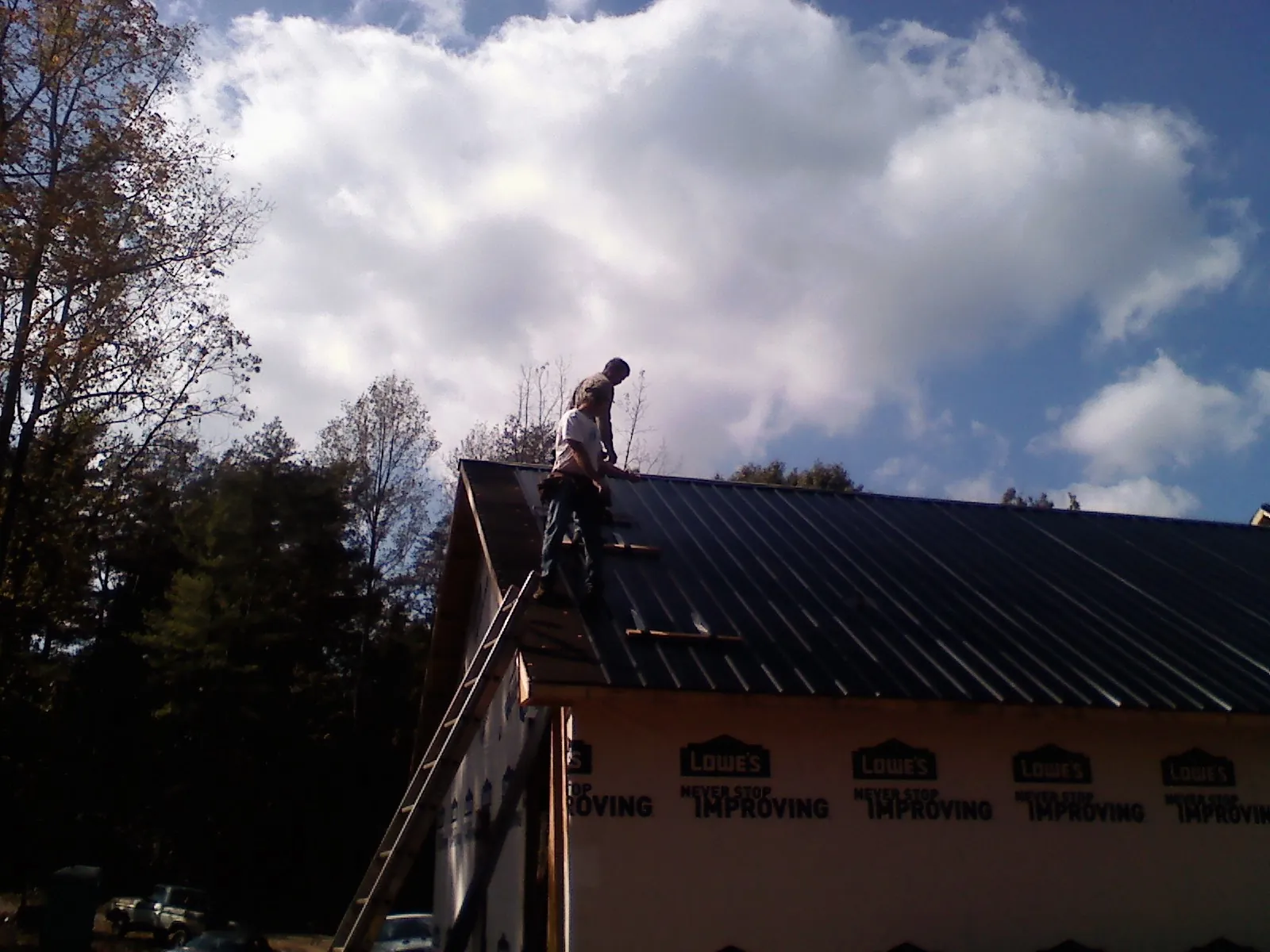 Roofer fastening dark metal panels high against a cloudy sky, from a Roof Inspection job in Tow