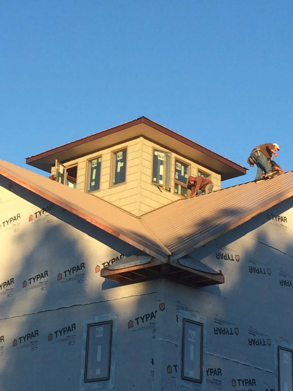 Roofers working around a rooftop cupola on a new metal roof at sunset — Roof Waterproofing in Tow by Roofing Brothers